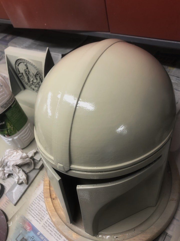 Casque de cosplay imprimé en 3D, poncé et recouvert d'apprêt gris, posé sur un plan de travail au milieu des pots de finition