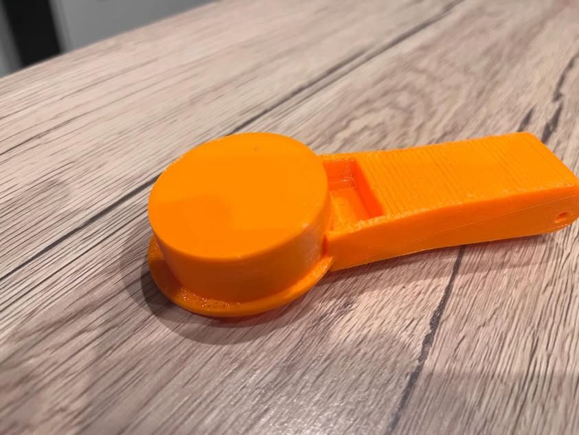 Pièce technique orange imprimée en 3D, forme fonctionnelle à bord nervuré, posée sur un plan de travail