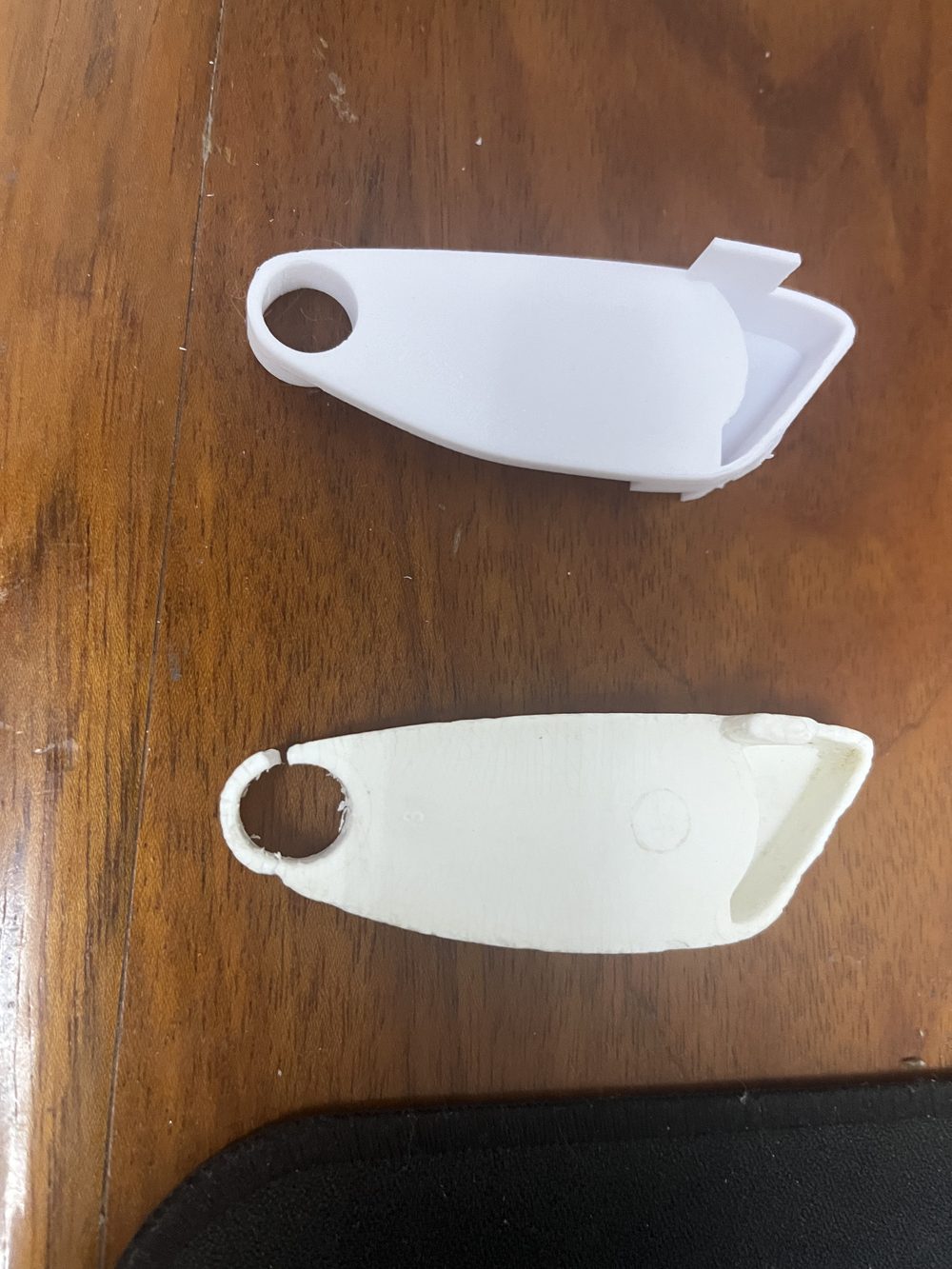 Deux moitiés d'une pièce plastique reproduite en impression 3D, posées sur un plan de travail en bois