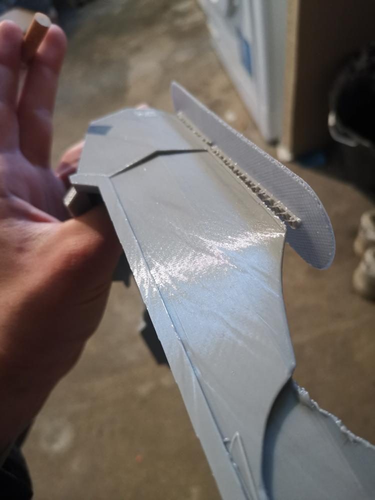 Pièce imprimée en 3D tenue à la main pendant son ponçage, strates d'impression encore visibles sur la tranche