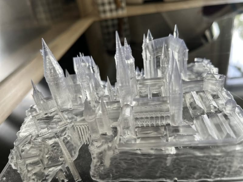 Château miniature imprimé en résine transparente, flèches et arcades finement détaillées, encore sur son support d'impression